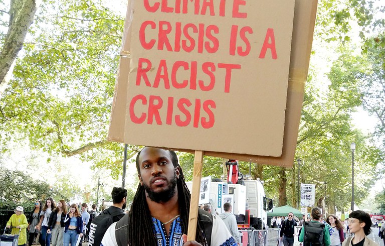 Foto: een man in Amerika demonstreert tegen klimaatracisme. Op zijn protestbord staat de tekst: Climate crisis is a racist crisis.