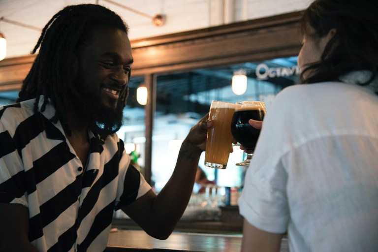Foto: 2 mensen drinken samen een biertje aan de bar, ze toosten.