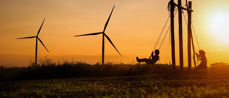 Kinderen schommelen bij windmolens tijdens zonsondergang