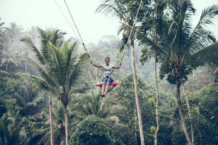 Lachende vrouw op een schommel tussen de bomen van een tropisch regenwoud