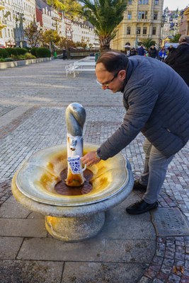 Een man tapt mineraalwater uit een bron op straat.
