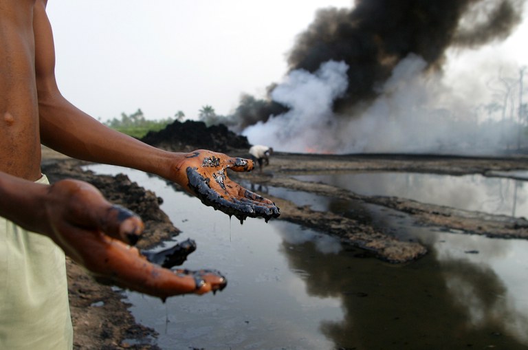 Foto: jonge man in Nigeria met olie op zijn handen die uit pijpleidingen van Shell is gelekt.