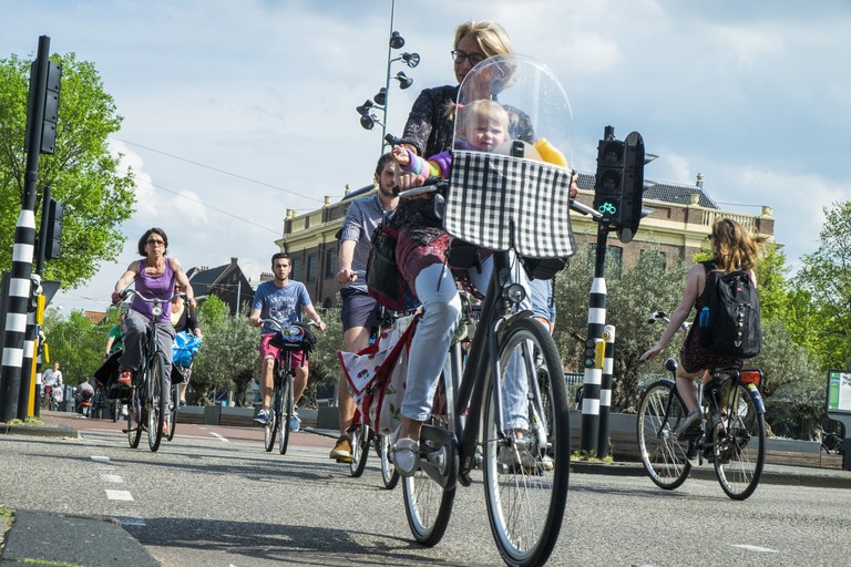 Foto van fietsende mensen in de stad, met op de voorgrond een moeder met haar kind in een zitje.