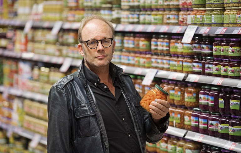 Keurmerken op voedsel voor duurzaamheid.jpeg Foto van een man in de supermarkt met een potje wortelen in zijn hand.