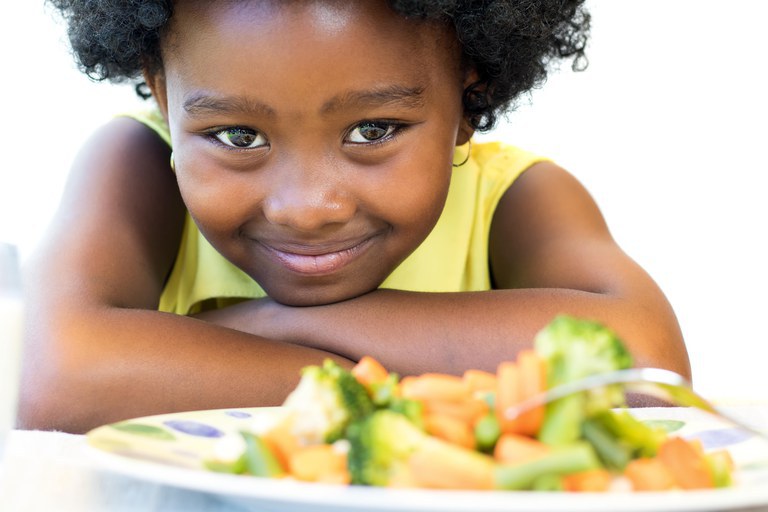 Foto van en vrolijk lachend meisje met een bord vol groente voor zich.