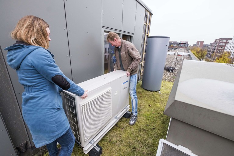 Warmtepomp duurzaam verwarmen - Milieudefensie.jpeg Foto van een vrouw en een man die een warmtepomt op het dak van een huis plaatsen.