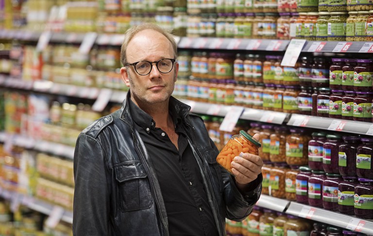 Foto van een man in de supermarkt met een potje wortelen in zijn hand.